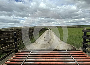 Lane with a cattle grid, leading toward a wind turbine, and a farm above, Bradley, UK