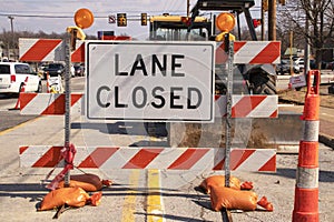 Lane Closed sign at messy construction urban intersection with sand bags traffic cones heavy equipment working and cars stopped at