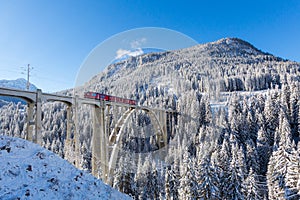 Red Rhaetian railway train on viaduct Langwies, sunshine, winter