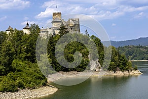 Lanscape view of a castle on the hill next to the lake with mountains in the background