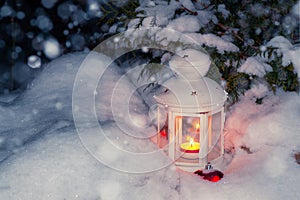 Lantern with a burning candle under a snow-covered Christmas tree in the courtyard of the house in the snowdrifts