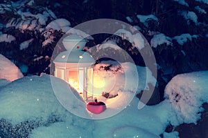 Lantern with a burning candle under a snow-covered Christmas tree in the courtyard of the house in the snowdrifts