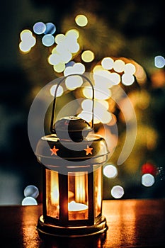 A lantern with a lit candle inside with bokeh lights on background