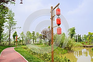 Lantern-shaped streetlamp by lakeside red path in sunny spring