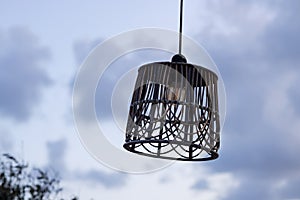 Lantern with wicker lampshade on double wooden pole and crossbar on seashore against cloudy sky