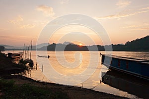 Laos fisherman with fishing wooden boat in the Mekong River at sunset. Simple life. Traditional Laos boat foregrounds. Beautiful