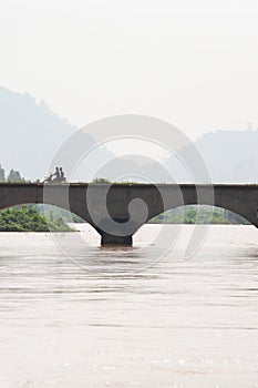 Laos man riding motorcycle crossing the bridge across Mekong River. The Mekong River is going overflow. Don Det Island, Si Phan
