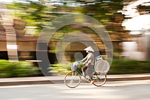 Laotian female street vendor riding bicycle with stainless tray on the street of Luang Prabang, Laos