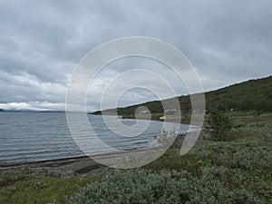 Lapland landscape at Virihaure lake with sami village Staloluokta houses and cottage, snow capped mountains and birch