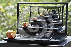 Laptop with apple and eyeglasses on garden table