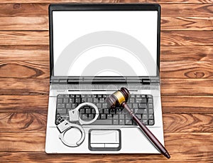 Laptop with blank display, handcuffs and gavel on wooden table