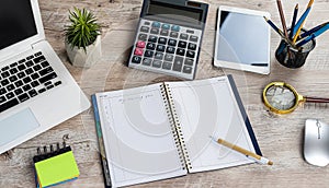 Laptop, blank notepad, pen calculator, reminder flower on office table