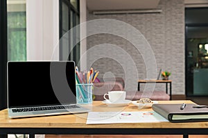 Laptop with blank screen, pencils, vase on table in home office. Workspace with laptop and office supplies