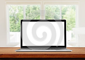 Laptop with blank screen on wooden table and blurry image of Living room in background.