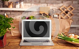 Laptop with blank screen on wooden table in the kitchen. Concepts of online grocery store