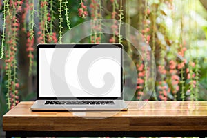 Laptop blank screen on wooden table red flowers green garden