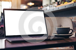 Laptop with blank white desktop screen and coffee cup on wooden table in modern cafe
