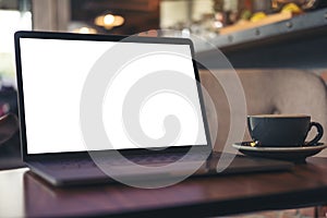 Laptop with blank white desktop screen and coffee cup on wooden table in modern cafe