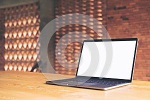 Laptop with blank white desktop screen on wooden table with concrete wall background