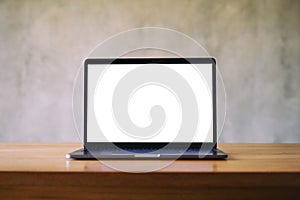 Laptop with blank white desktop screen on wooden table with concrete wall background