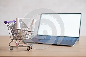 Laptop with blank white screen and miniature shopping cart full of medicines. Online pharmacy concept. Website for