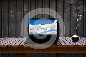 Laptop with blue sky and cloud on screen on wooden table and a cup of coffee.