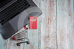 Laptop, calculator and shopping cart on wooden table. Online Shopping Concept