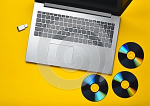 Laptop, CD drives, USB flash drive on a yellow background. Modern and outdated digital media