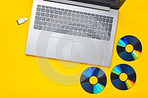Laptop, CD drives, USB flash drive on a yellow background. Modern and outdated digital media.
