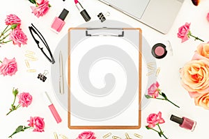 Laptop, clipboard, roses flowers, cosmetics and accessories on white background. Flat lay. Top view. Feminine office or blogger co
