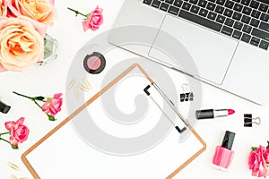 Laptop, clipboard, roses flowers and cosmetics on white background. Flat lay. Top view. Woman freelancer composition