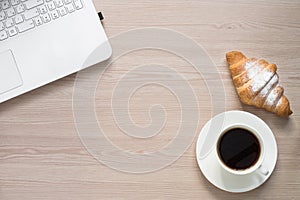 Laptop, coffee and croissant at desk table.