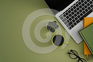 Laptop, coffee cup, eyeglasses and books green background with copy pace.