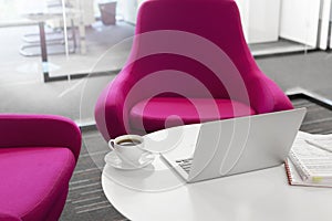 Laptop with coffee cup and file on table by pink chairs at office