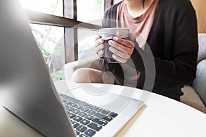 Laptop and coffee cup in girl`s hands sitting at home