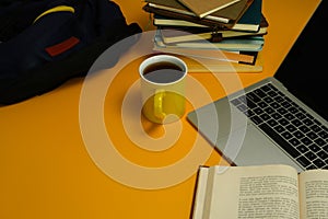 Laptop, coffee cup and stack of books and backpack on yellow background. Online learning, back to school and education