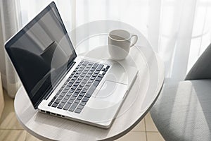 Laptop and coffee cup on table and chair in bedroom