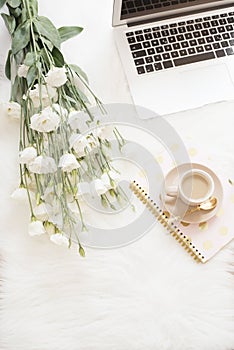 Laptop, coffee, notebook and a large bouquet white flowers on the floor on a white fur carpet. Freelance fashion comfortable femin