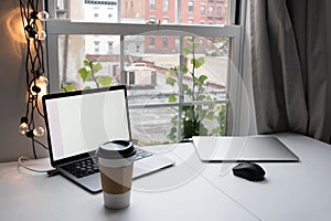 Laptop computer with blank screen and coffee cup on table at home