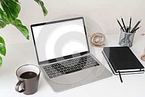 Laptop computer with blank screen for mockup on modern contemporary workspace desk with coffee cup and office supplies. Home