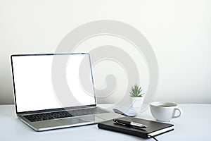 Laptop computer blank screen on white office desk table with coffee cup and notebook