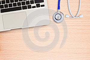 Laptop computer with blue stethoscope on wooden desk.