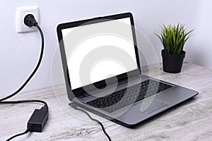 Laptop, computer is charging from a 220-volt outlet on a desk near the wall. Energy, accumulation. Mockup