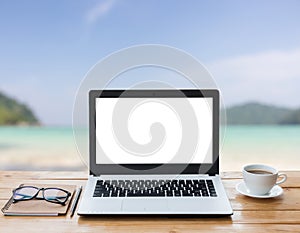 Laptop computer and coffee on wood workspace and the beach