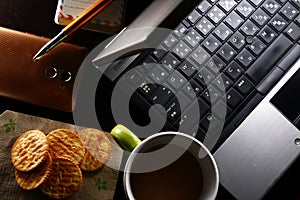 Laptop computer, cup of coffee, ballpen, notebook, crackers, and a smartphone