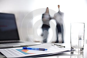 Laptop computer with folder on desk , two businesspeople standing in the background