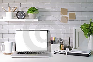 Laptop computer, houseplant, coffee cup, picture frame and supplies on white table. Home office