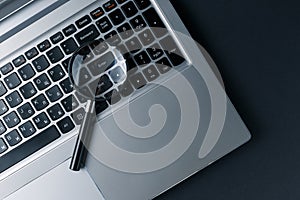 Laptop computer with magnifying glass on dark background, concept of search. Internet security conceptual image