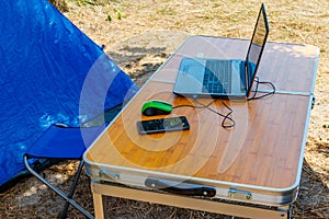 Laptop with computer mouse and smartphone on a folding picnic table in a camping. Working while traveling. Freelance work