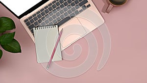 Laptop computer, notepad, coffee cup and houseplant on pink background. Top view with copy space